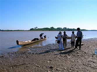 people on a broad river beach with a narrow, long wooden boat